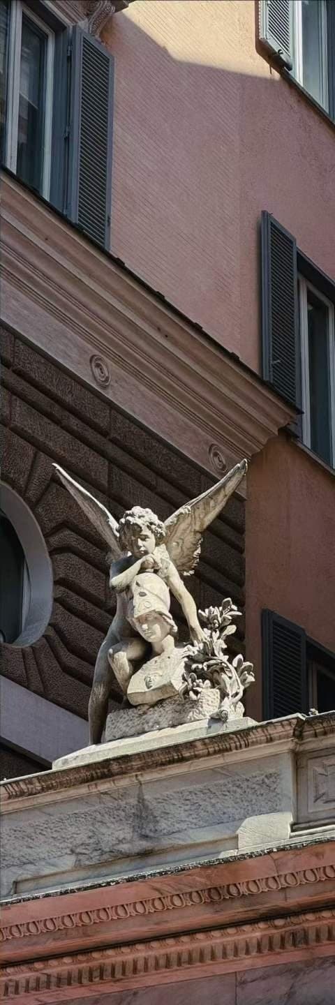 A carved stone angel on the corner of a pink stucco building against a clear sky.