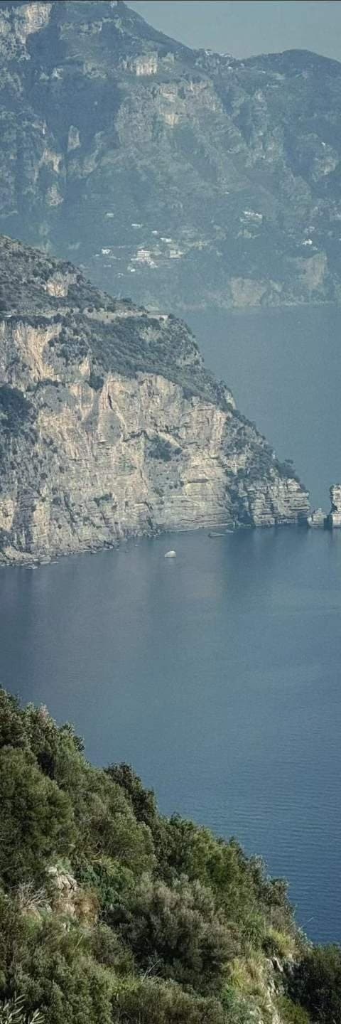 A limestone coast dropping steeply into deep blue water, terraced houses on the ridge above.