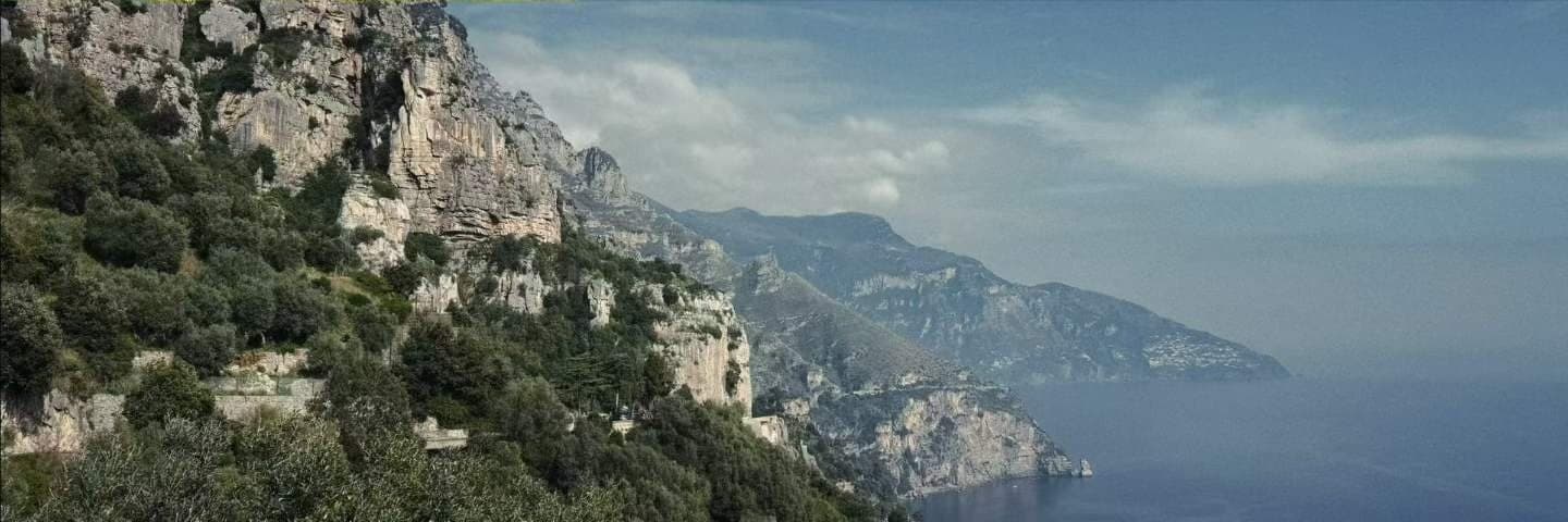 A long stretch of cliff coast in haze, the road cut into the rock a thin line above the water.