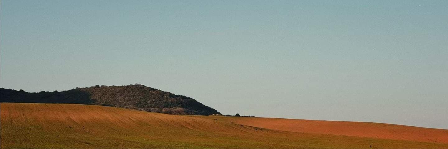 A ploughed ochre field running to a low dark hill under a graded evening sky.