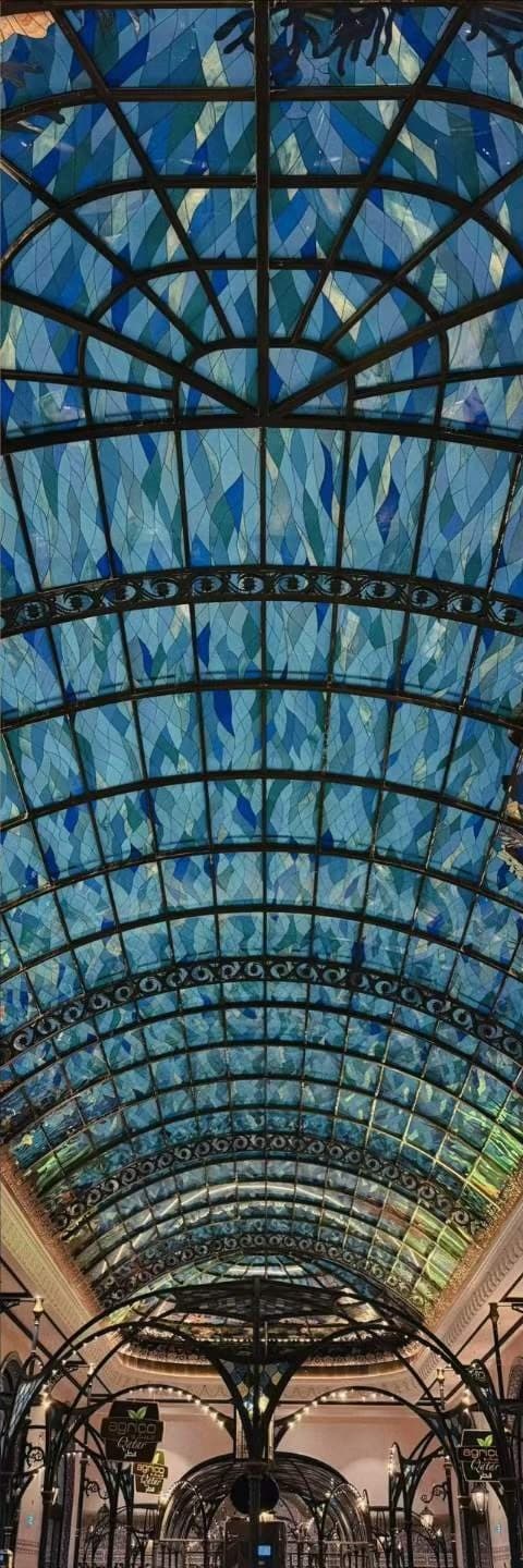 A blue glass barrel roof over an iron arcade, seen from below along its length.