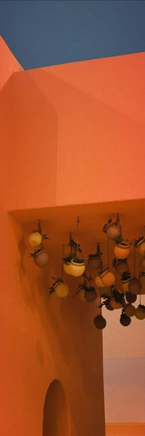 Glazed pots in yellow and terracotta hung against a bright orange rendered wall.