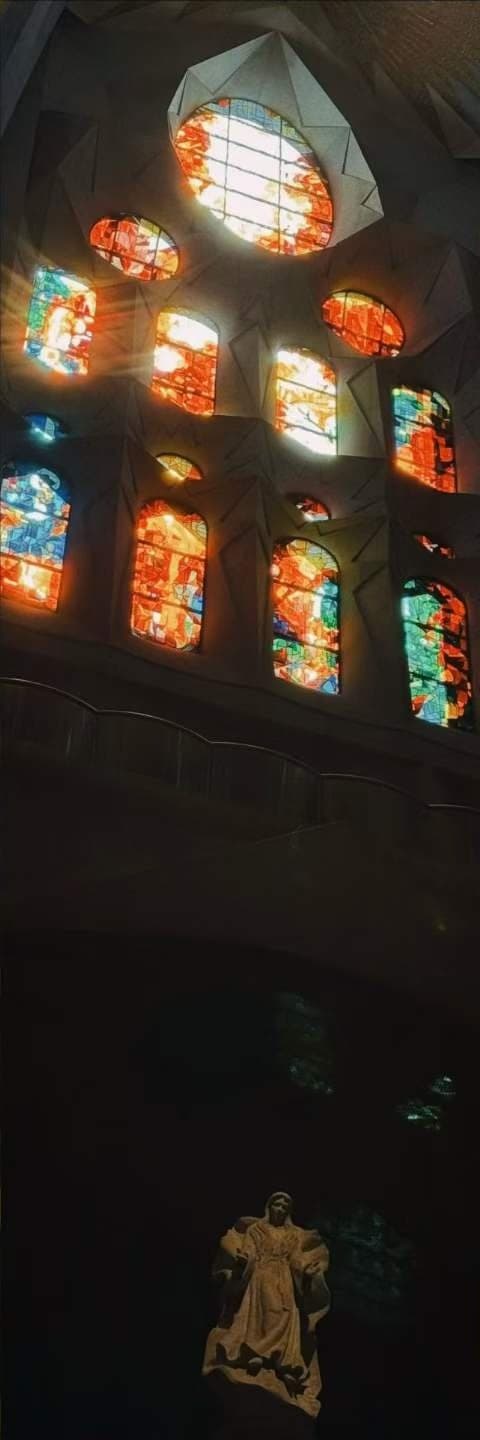 A wall of stained glass in reds, oranges and blues burning against a dark interior.